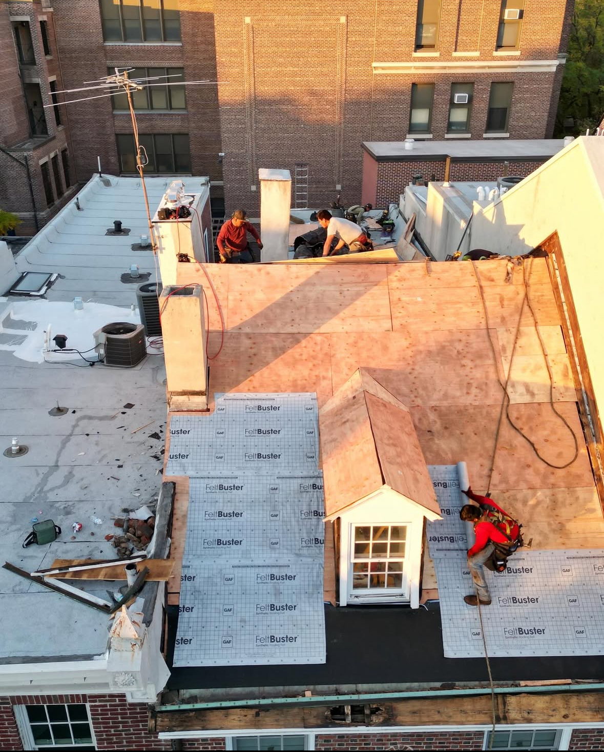 A J. Parker Contracting crew laying synthetic underlayment over fresh decking at golden hour, photographed by drone